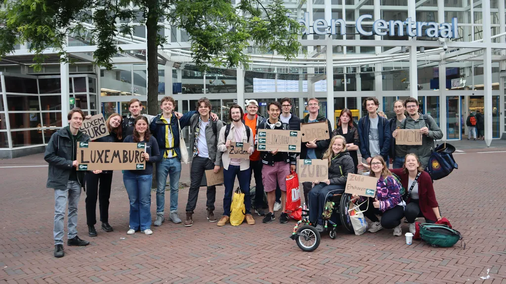 Groepsfoto van lifters die hun liftbordjes omhooghouden, samen voor Leiden Centraal.
